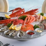 Best Sauces and Dips for Seafood Platters 3 A beautifully arranged seafood platter featuring lobster tails, crab legs, jumbo shrimp, scallops, mussels, and oysters, garnished with lemon wedges and parsley on a decorative tray with crushed ice