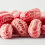 Boston Baked Beans Candy 5 A close-up view of glossy, red Boston Baked Beans candy in a vintage glass jar on a wooden countertop.