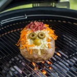 Crispy grilled baked potato with butter and chives on a BBQ grill.